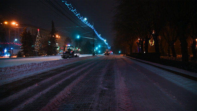Large snow tractor at work on the evening streets of the city