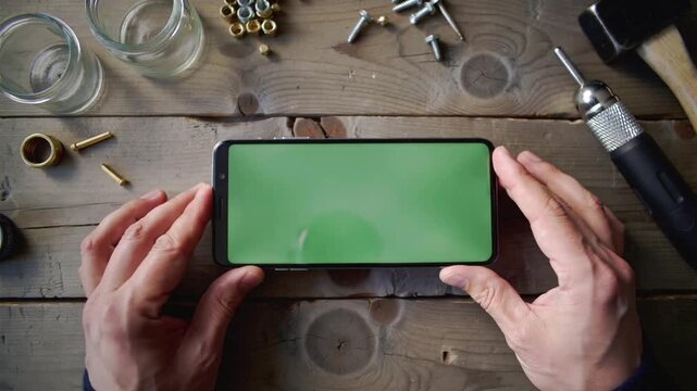 Hands touching green screen on smartphone surrounded by tools and hardware mobile phone chroma key