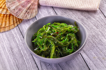 Japanese seaweed salad Chuka with sesame seeds and chili in a white bowl on a wooden table.