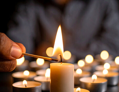 Mano encendiendo una vela con una cerilla de llama brillante en ambiente oscuro y velas encendidas, concepto de calma, espiritualidad, ritual y momento &iacute;ntimo de luz o dia de todos los santos