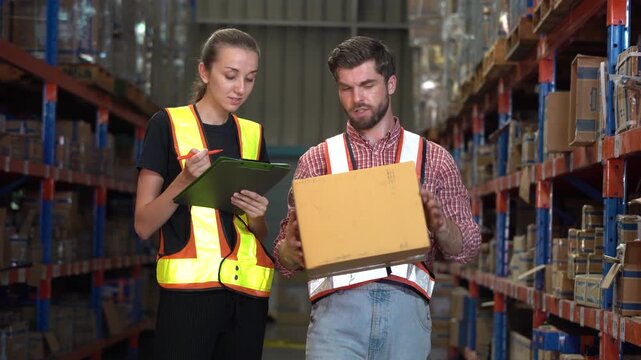 Caucasian man and woman warehouse workers talking. Man checking box he is holding while woman holds clipboard. Professional logistics team inspecting package in industrial distribution center.