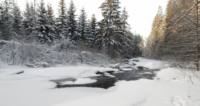 Tranquil, partially frozen river flowing through a snow-covered forest during winter, Matarinkoski, Vantaa, Finland, Europe.