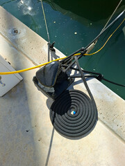 Fototapeta premium Close view of a black cast iron mooring bollard with coiled nautical rope on concrete pier by blue sea water on a sunny day