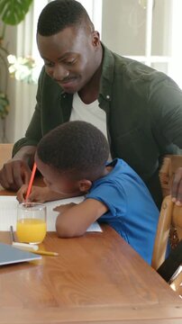Vertical video: Leaning son, green-shirt dad guiding hand with red pencil at home learning