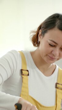 Vertical video: Grabbing shears, woman in yellow overalls trimming basil at kitchen counter to cook