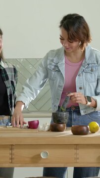 Vertical video: Pouring oil, pair grinding herbs in mortar at home, one wearing denim, making paste