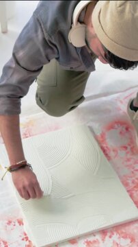 Vertical video: Inspecting Indian artist peeling and scraping canvas in studio with scraper, beanie