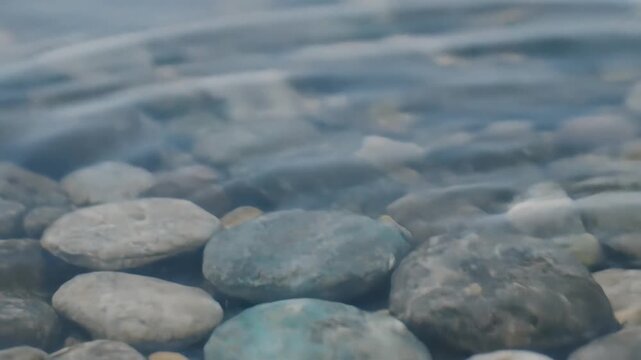 Closeup of water ripples over smooth pebbles in clear shallow water.