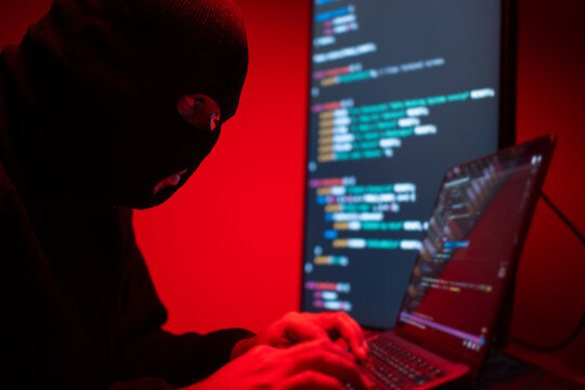 Hacker in balaclava with an obscured face is stealing data, representing cybercrime, hacking, dark web activity, and online security threats. Cyber Security concept.
