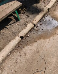 Fototapeta premium Concrete curb beside wooden bench and dirt walkway forming urban park pathway composition in daylight environment