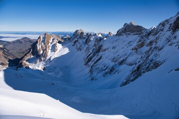 Obraz premium Ski descent from the Säntis in the Appenzell Alps. Ski tour in the Alpstein region. From Schwägalp to Toggenburg. Ski tour in rugged terrain. Skier enjoys the view of the snow-covered mountains