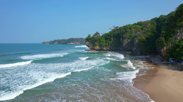 Aerial drone footage of Sawarna beach edge, in Banten, Java island, Indonesia, with waves, blue waters, cliffs with forests on it, with many caves inside like the famous Goa Langir