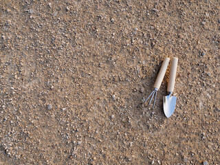 Gardening tools including a trowel and hand fork resting on dry, sandy soil in a garden setting. Small gardening tools on soil background, spring garden preparation for planting vegetables