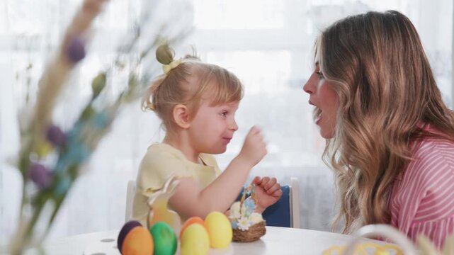 Young girl and mother share joyful Easter moment. Mother laughs with delight as daughter smiles brightly. They sit at table decorated with colorful eggs. Scene radiates warmth, family bonding