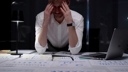 Stressed businessman suffering from overwhelming burnout and work overload, working late into the...