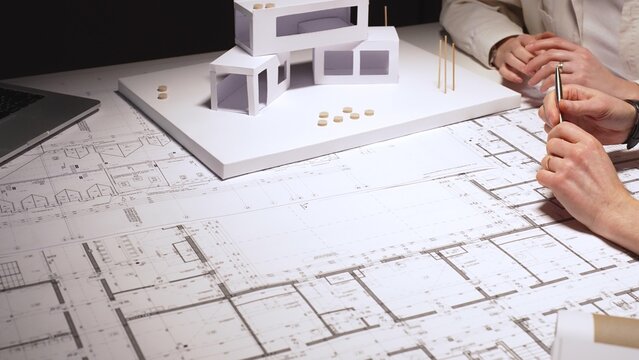 Architects collaborating on architectural blueprints, reviewing construction plans, and designing a modern building using a scale model in a professional office workspace