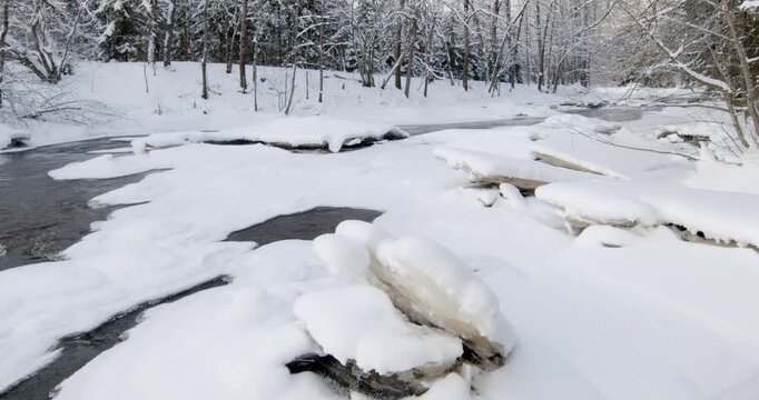Tranquil, partially frozen river flowing through a snow-covered forest during winter, Matarinkoski, Vantaa, Finland, Europe.
