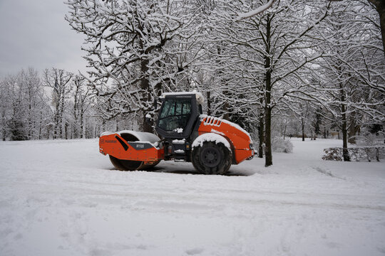 Vienna, Austria- Feb 21, 2026: A snow-covered park features a Hamm H121 roller machine clearing white snow under trees, symbolizing winter maintenance and urban improvement.