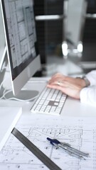 Architect working at desktop computer, checking blueprints and design plans for a new engineering...