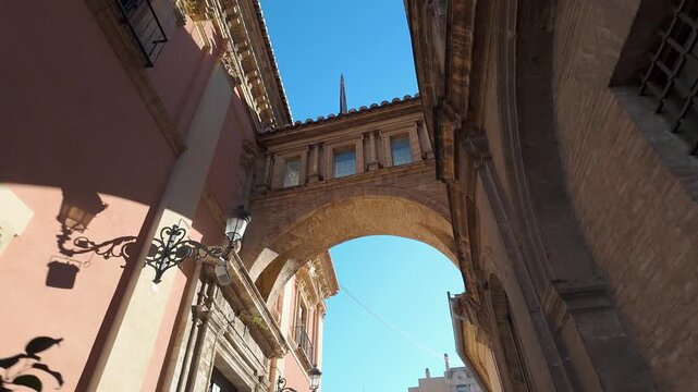 Arch between historic buildings in the city center of Valencia on sunny day, Spain.