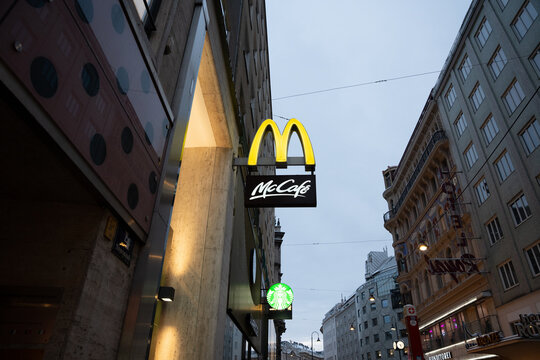 Vienna, Austria- Feb 21, 2026: A McCafe sign illuminated at dusk in Vienna's historic district, showcasing the urban atmosphere and multiple cafe options in the city.