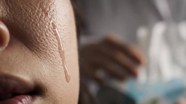 Close-up of a child's face with a tear running down their cheek, blurred background with a person in the distance, conveying a sad and emotional mood.