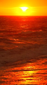 Sunset ocean waves glowing orange sun sets over the restless sea while rhythmic tides wash the beach during a peaceful golden hour