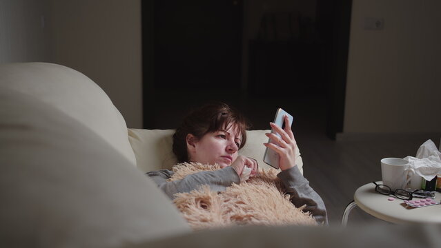 sick brunette woman lies on the sofa and use a phone in the evening, have fun and enjoy