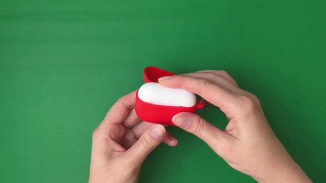 A woman's hands place a silicone protective case on a pair of wireless headphones against a green background. Conceptually, this refers to the protection of gadgets, electronic accessories.
