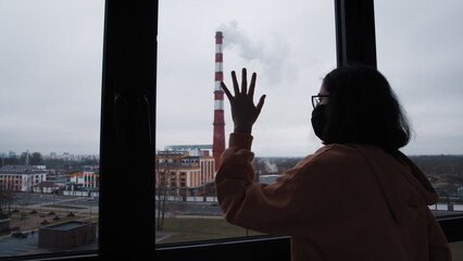 brunette girl in a mask stands on the balcony, smoke comes from the chimney and pollutes the air, environmental disaster, pollution of the planet, have fun and enjoy © vla