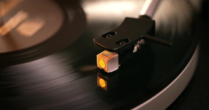 Detailed close-up of a turntable tonearm with white cartridge headshell, positioned over a black vinyl record on the platter, highlighting audio equipment precision.