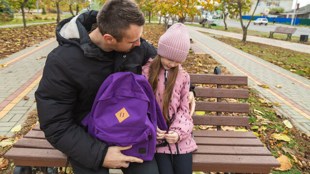 Father meets child from school. Dad with daughter sitting on beanch