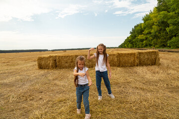 Two small children playfully run across a prepared field, with bales of hay.