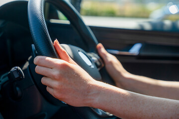Hands grip steering wheel while driving on a sunny day in a car on an open road