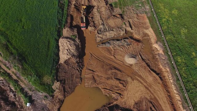 Maquinaria en acci&oacute;n y su huella: dumper retrocede para cargar el remolque por la  excavadora en la cantera. Impacto ambiental visible