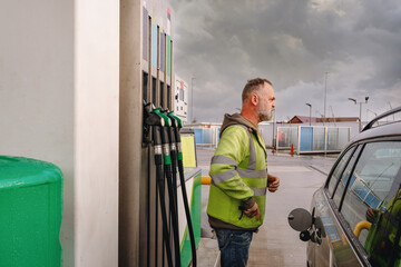 Sad Worker fills car at gas station under cloudy sky in the late afternoon © Iryna