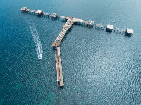 Aerial view of a boat speeding past an abandoned pier over a turquoise ocean