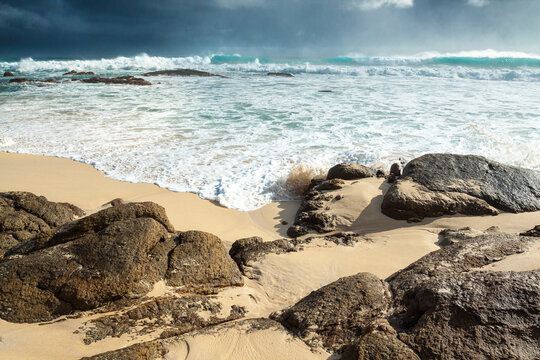 Low angled view of a dark stormy sky over rough waves breaking over shoreline rocks