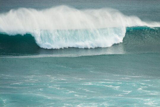 Spray blowing off the crest of huge wave breaking in the ocean