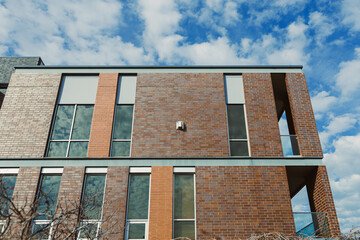 Brick building stands under a cloudy sky in an urban area during the daytime while showcasing modern architectural design elements and large windows © Zoryna