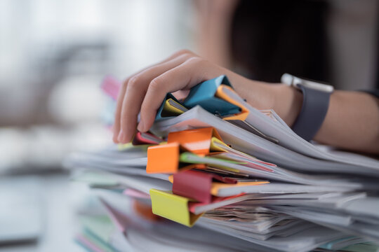 Hand organizing a large stack of paper documents, each section secured by colorful binder clips, representing paperwork management, heavy workload, and office organization