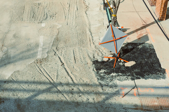 Construction work occurs on a city street with a traffic sign and fresh asphalt in the early afternoon near a residential area in fall