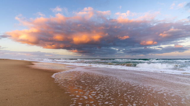 Low angled view of a colourful storm clouds over waves breaking in a sandy beach at twilight