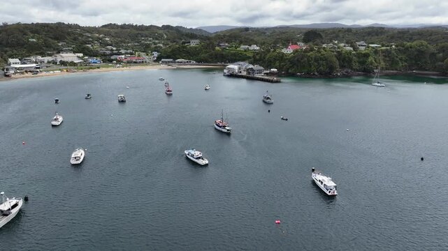 Aerial landscape view, flying across Halfmoon Bay toward Oban, a settlement on Stewart Island, New Zealand, with Ferry Terminal, beach and hilly wooded landscape in background 4k aerial video footage 