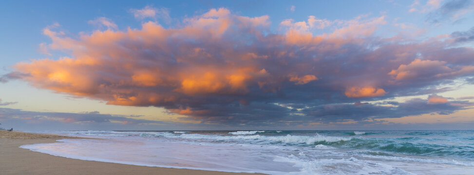 Low angled view of a colourful storm clouds over waves breaking in a sandy beach at twilight