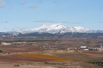 Naklejka premium Snowy Mountain Range Overlooking Autumn Vineyards and Village