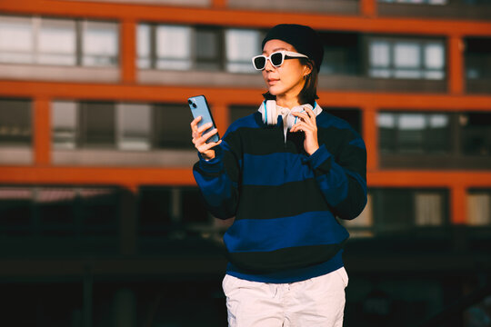 Young asian woman using smartphone with headphones in urban environment