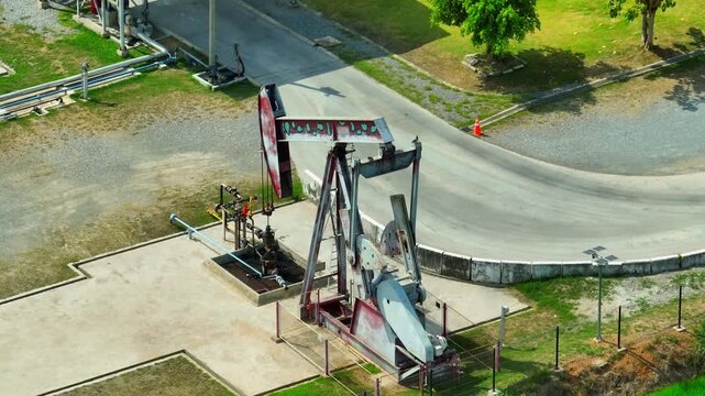 Aerial view from a drone showing a pumpjack extracting oil at a well site, with pipeline networks and industrial equipment representing petroleum extraction infrastructure.
