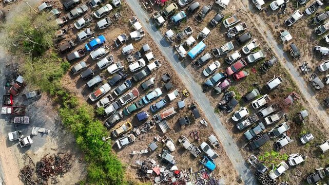Aerial drone view of a car scrapyard filled with hundreds of abandoned vehicles arranged along dusty lanes, illustrating automotive recycling, scrap metal recovery, and end-of-life vehicle management.