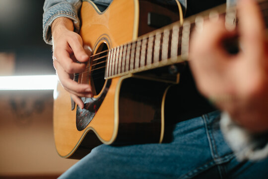 Young musician composing music playing acoustic guitar at home